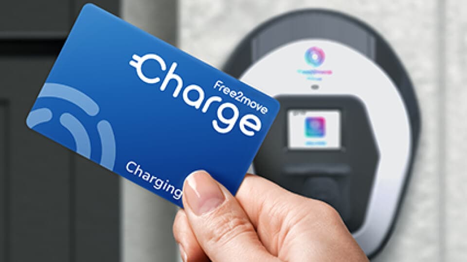Hand hält eine blaue Free2Move Charge kontaktlose Karte in die Nähe einer Elektrofahrzeug-Ladestation.